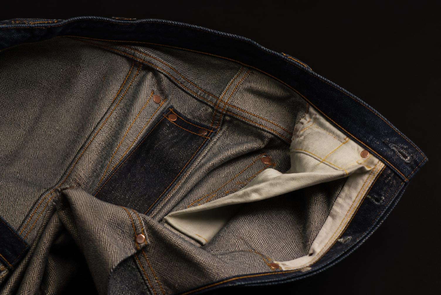 Interior de una prenda de denim con costuras y remaches visibles.