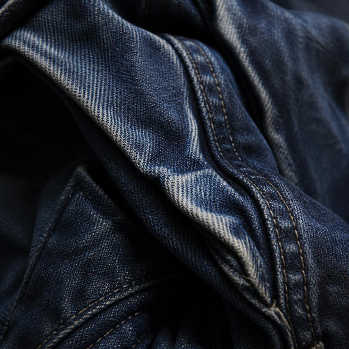 Macro de denim índigo usado, con pliegues y costuras visibles.